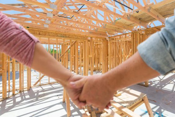 Couple Holding Hands Looking At Their New House Framing