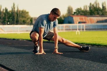 Young athlete stretches on the track during evening...