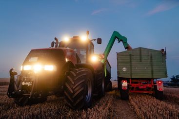 Tractor on harvested grain field during dusk