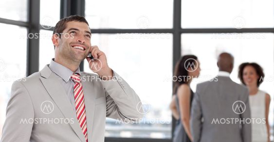 Young businessman holding a phone at workplace with his colleagues