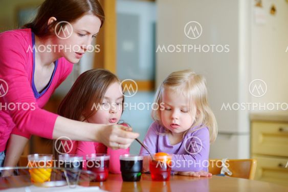 Young mother and her two daughters painting Easter eggs