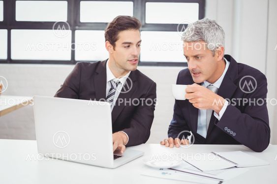 Businessman having coffee while working with colleague