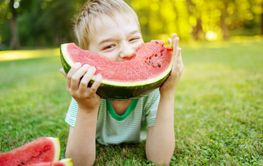 Cute child lying on the grass and eating juicy slice of...