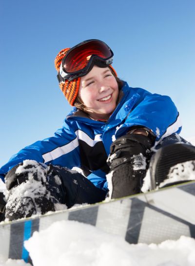 Young Boy Sitting In Snow With Snowboard