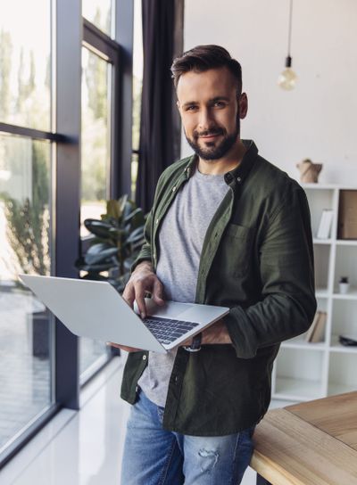 Handsome smiling bearded man using laptop while standing...