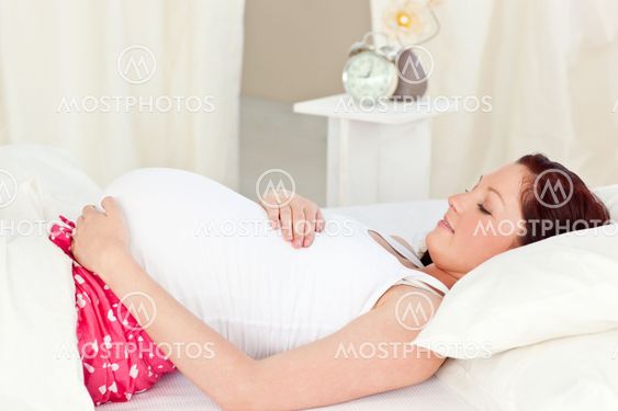 Portrait of a happy pregnant woman lying on bed and touching her belly