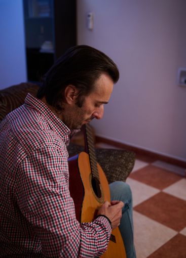 Focused man holding an acoustic guitar sitting indoors...