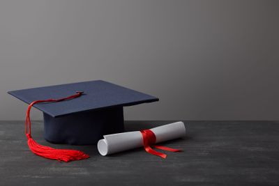 Diploma and academic cap with red tassel on dark surface...