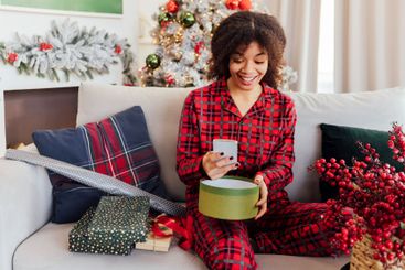 Young African woman in red plaid pajamas is sitting on...