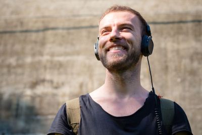 hipster modern stylish blonde man listening music in park