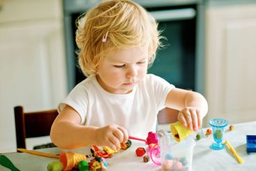 Adorable cute little toddler girl with colorful clay at...