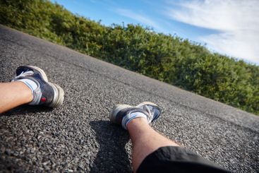 Man, legs and runner relaxing on road, exhausted and...