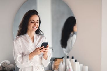 Brunette woman enjoying skin care routine while using...