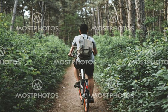 Young man with backpack cycling on a forest path, active...
