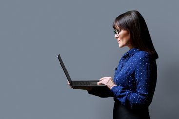 Smiling middle aged woman using laptop on gray background