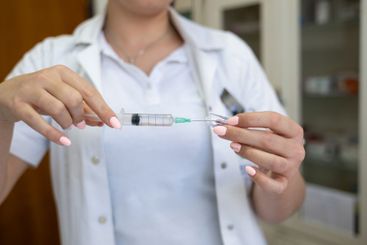 A focused nurse in a white lab coat carefully prepares a...