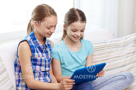 happy girls with tablet pc sitting on sofa at home