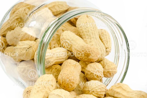 Close up of a glass jar full of unpeeled peanuts on a white background