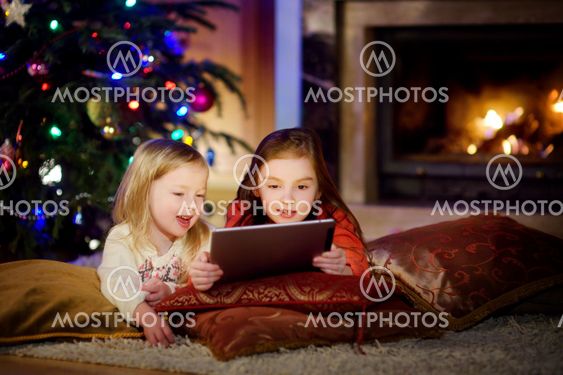Two cute little sisters using a tablet pc by a fireplace...