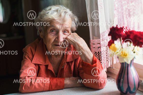 Portrait of elderly woman near window in the house.