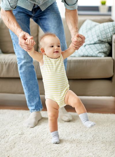 father helping baby daughter with walking at home