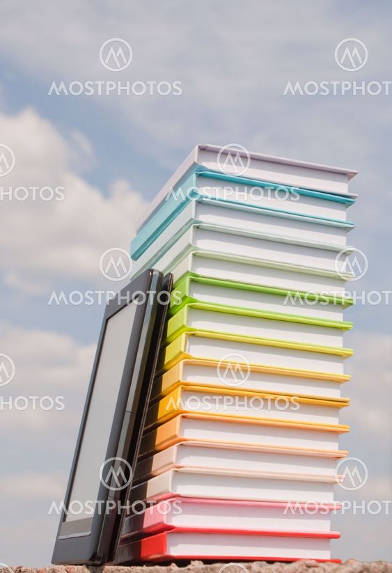 Stack of colorful books and electronic book reader outdoors