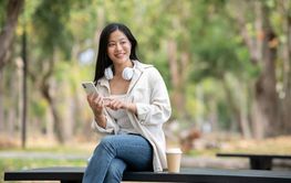 A smiling asian woman holding phone and looking around...