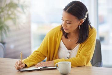 Notebook, coffee and woman writing in home with study...
