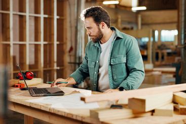 Carpenter, laptop and plans with wood to measure for...