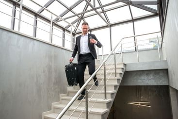 Businessman holding suitcase running on stairs in modern...