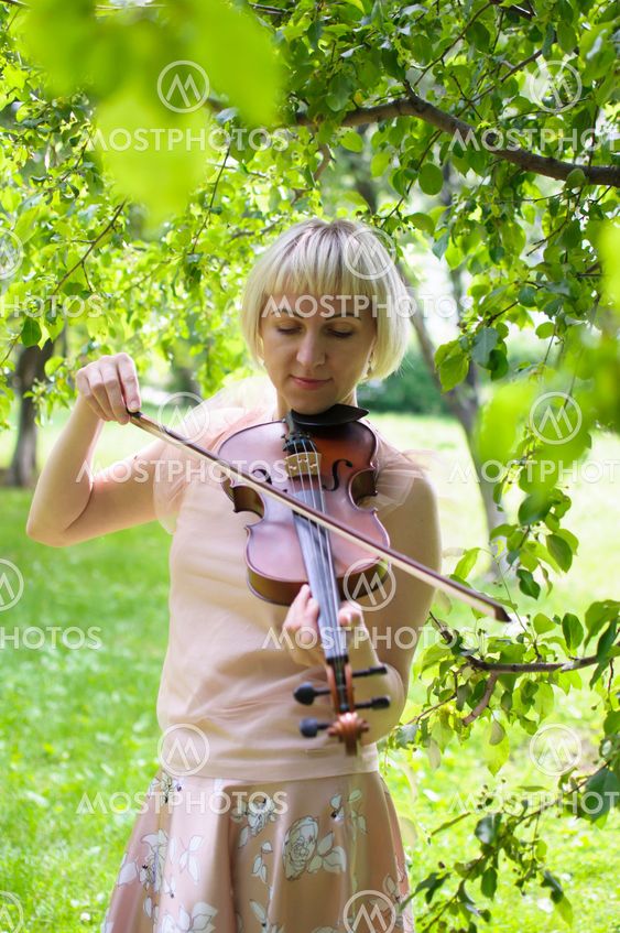 The Russian woman plays a violin in the park in the summer.