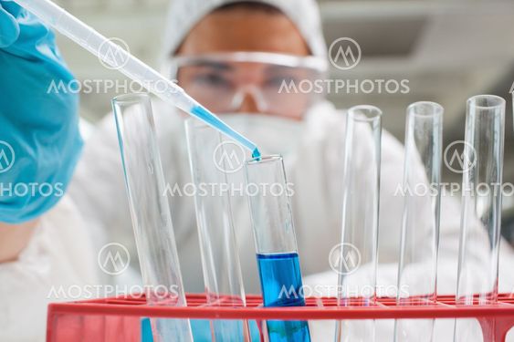 Protected science student dropping blue liquid in a test tube