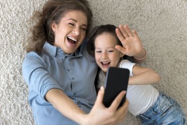 Laughing millennial mother little daughter cuddle on...