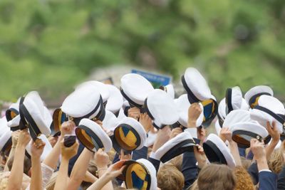 Hands holding many swedish white graduation caps, green...