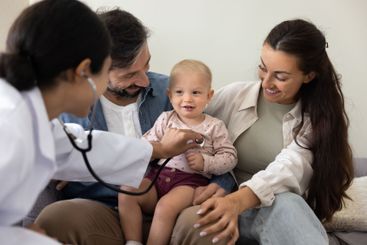 Female pediatrician visiting couple of parents holding...