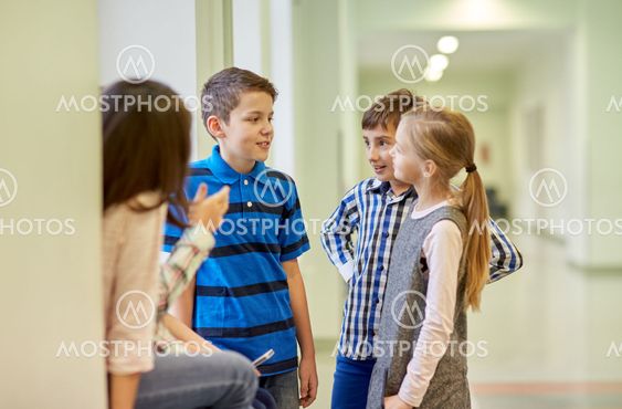 group of smiling school kids talking in corridor