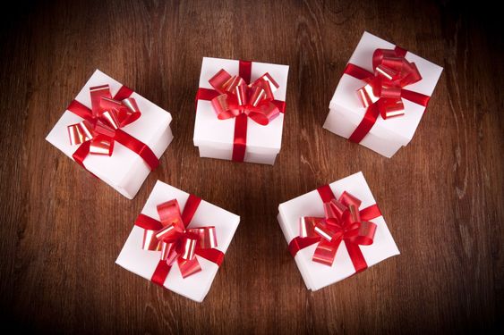 five white festive gift boxes with red bows on a wooden...