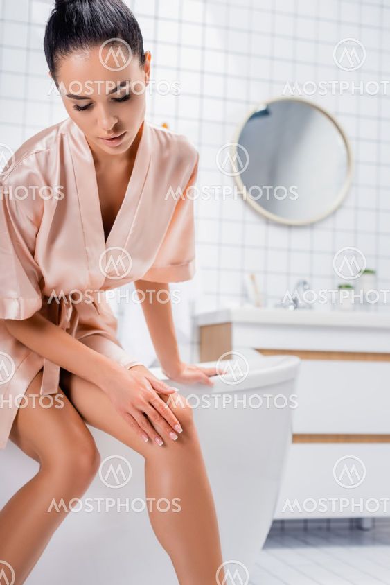 Young woman in satin bathrobe touching knee while...