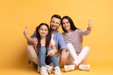 A cheerful family of three poses together with thumbs up