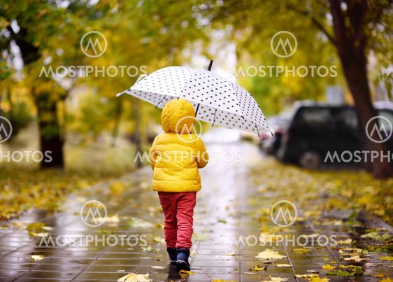 Little child walking in the city park at rainy autumn day