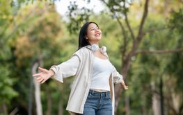An asian woman is smiling while standing with open arms...