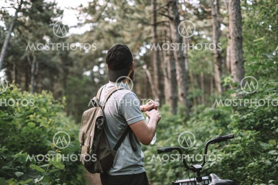 Young man with backpack cycling on a forest path, active...
