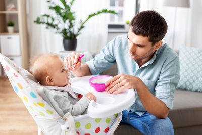 father feeding happy baby in highchair at home