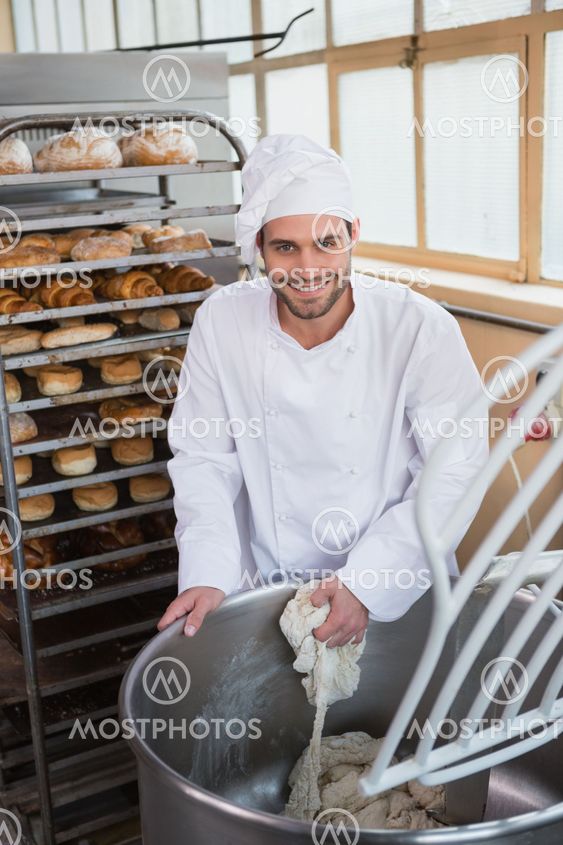 Smiling baker preparing dough in industrial mixer