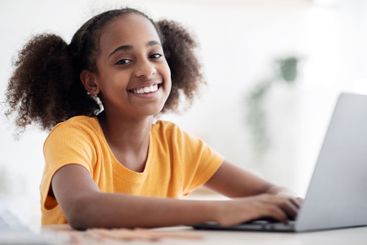 Cheerful black girl studying online, using laptop,...