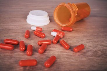 An open orange of brightly coloured pills spilled onto a...