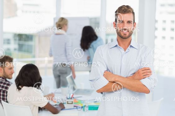 Handsome man smiling at camera while his colleagues are working