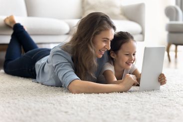 Young mom little daughter lie on carpet use digital tablet