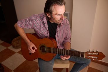 Man playing an acoustic guitar indoors wearing a casual...