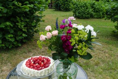 Jordgubbstårta och sommarblommor på ett bord i en trädgård